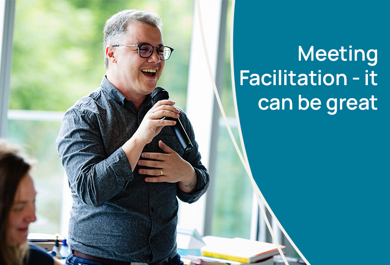 A man stands in front of a window speaking into a microphone looking joyful. The text reads, Meeting Facilitation - it can be great.