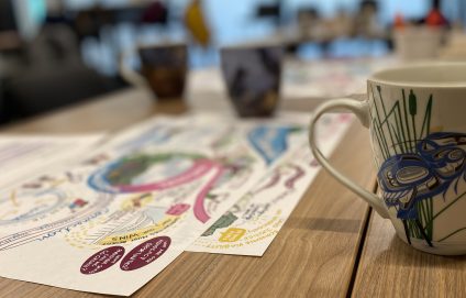 image of printed graphic recordings on a conference table with mugs next to it 